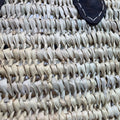 Detalle de capazo de palma grande con asas de cuero, ideal para playa y uso diario.