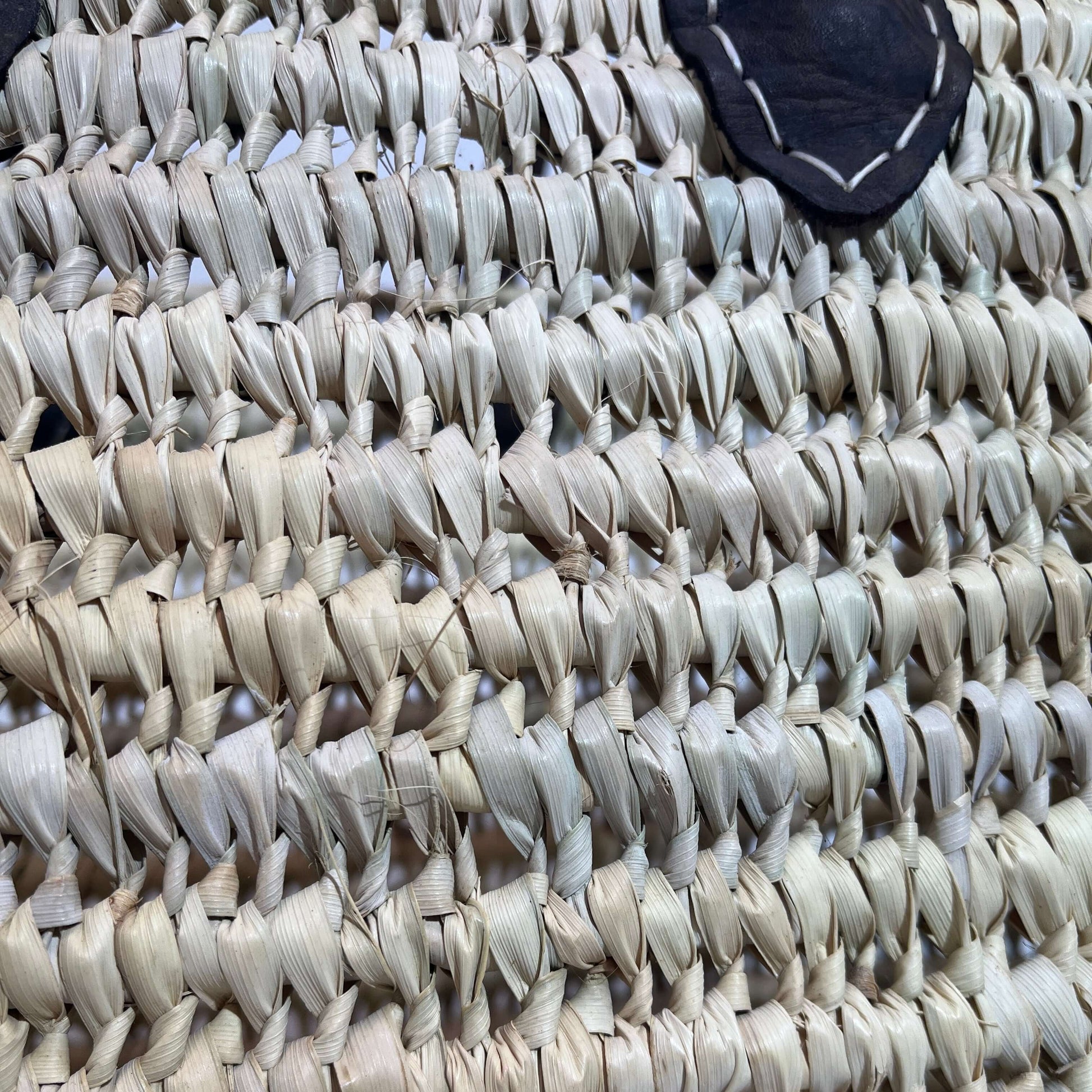 Detalle de capazo de palma grande con asas de cuero, ideal para playa y uso diario.