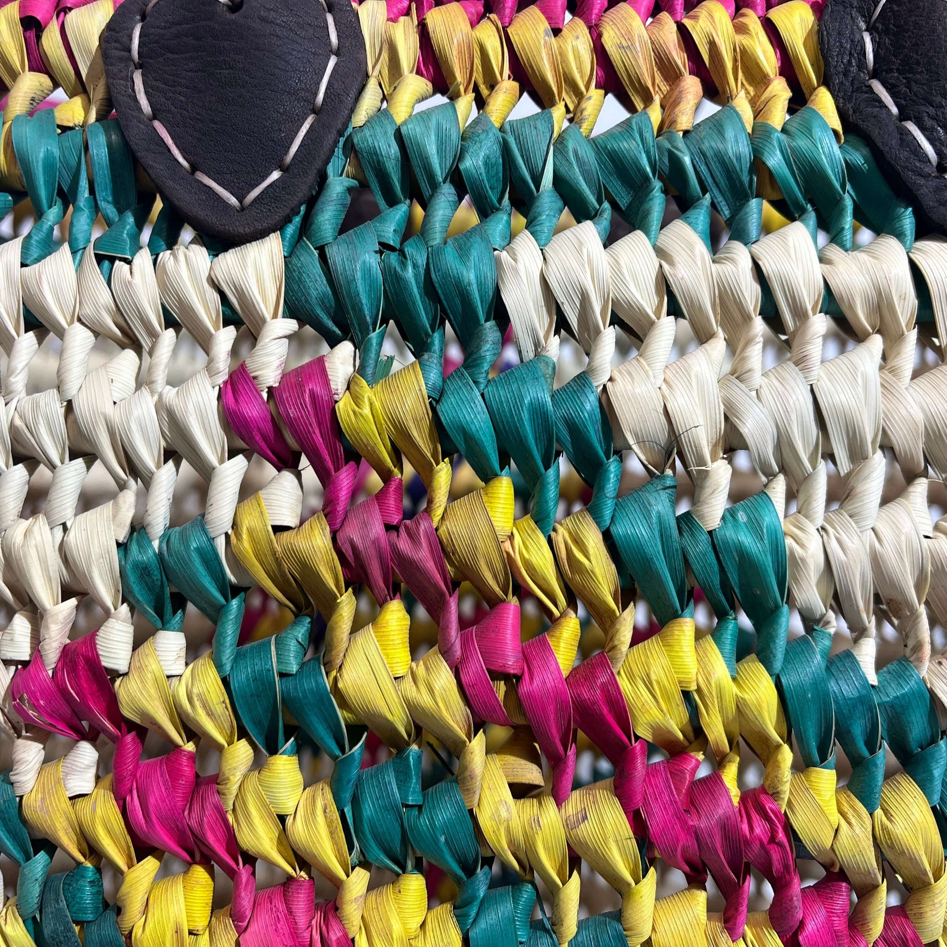 Colorful woven fabric of a capazo de playa, featuring pink, yellow, and teal strands with leather accents.